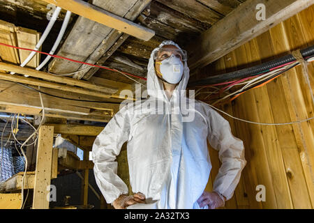 A close up view of a man standing indoors wearing hooded boiler suit, protective goggles and air filtration mask during an inspection of a domestic building. Stock Photo