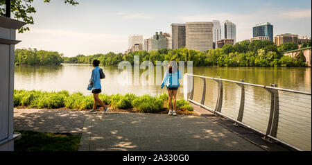 Two women standing by river in blue coats with office buildings in the background Stock Photo