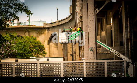 Two workers with hard hats in a bucket working on a bridge Stock Photo