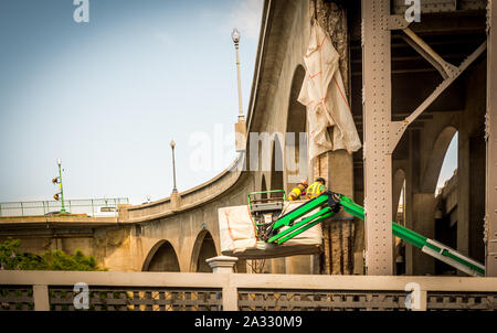 Two workers with hard hats in a bucket working on a bridge Stock Photo