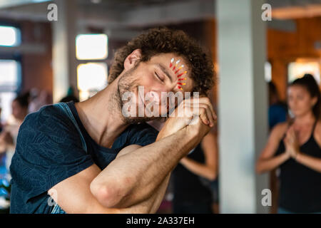 A young and spiritual Caucasian guy is seen up close, resting head on clasped hands with locked arms. Relaxed pose during 108 salutations to the sun. Stock Photo