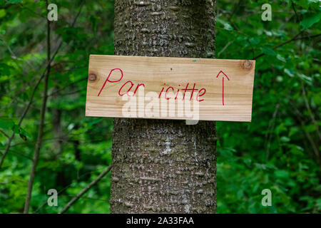 A small French sign, saying around here, is seen with a red arrow pointing towards a woodland trail near a campsite. Stock Photo