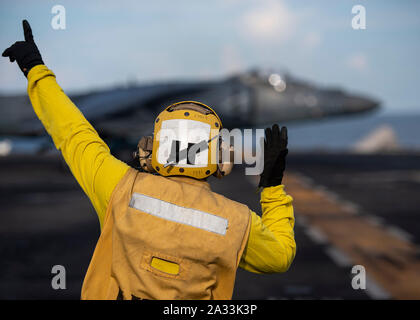191004-N-PM193-1050    SOUTH CHINA SEA (Oct. 4, 2019) Aviation Boatswain’s Mate (Handling) 3rd Class Jeandree Cespedes, from New York, assigned to the amphibious assault ship USS Boxer (LHD 4), signals an AV-8B Harrier II, attached to Marine Medium Tiltrotor Squadron (VMM) 163 (Reinforced), on the ship’s flight deck during Tiger Strike 2019. Malaysian Armed Forces were joined by U.S. Marines and Sailors for exercise Tiger Strike 2019 where both forces participated in jungle survival, amphibious assault, aerial raids, and combat service support training and cultural exchanges. The Boxer Amphibi Stock Photo