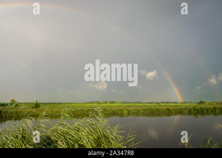 Bright colorful double rainbow over the dutch countryside near Gouda, Holland. The rainbow is reflected in the water of the canal. Stock Photo