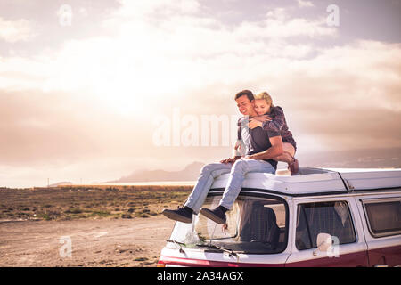 Young couple in love enjoying the travel on a vintage van during a golden sunset in a scenic place together hugging and smiling - youth people in outd Stock Photo