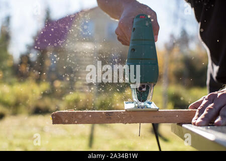 Man cuts wood product using an electric jigsaw joinery in the sun on a warm summer day outdoors. Stock Photo