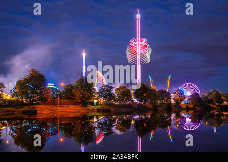 Germany, Colorful illuminated big wheel and rollercoaster of giant swabian fair called cannstatter wasen in stuttgart bad canstatt reflecting in water Stock Photo