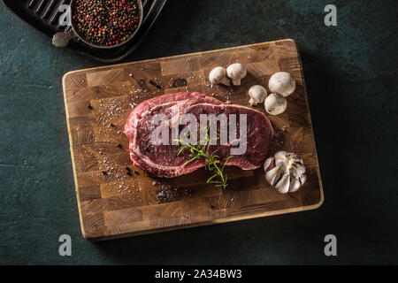 Rib Eye steak salt pepper spices garlic and mushroom. Raw beef meat on butcher board - top of view Stock Photo