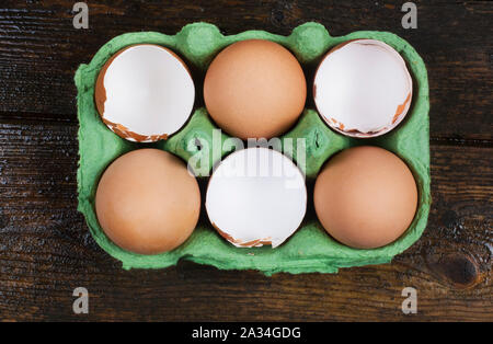 Studio shot of cracked, empty chicken egg shells in an egg box on a dark wooden background - John Gollop Stock Photo