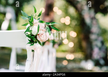 Decorated chairs for guests at the wedding little bouquet on a blurry background of burning lights. Wedding floristics for a modern wedding in the par Stock Photo
