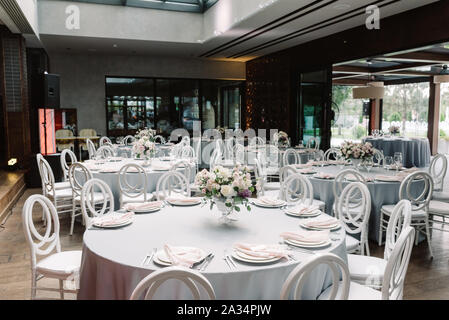 A restaurant hall filled with beautiful round tables for guests of the groom and bride at the wedding. Luxury tables with white tablecloths Stock Photo
