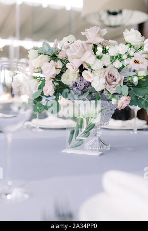 Stylish decoration of modern wedding with fresh flowers and table number on a small glass stand. Festive large table decorated with flowers for a sole Stock Photo