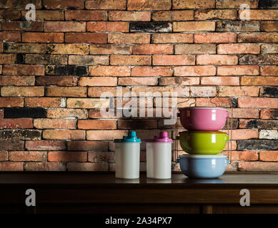 Colorful tiffin carrier and plastic cans on wooden cupboard in kitchen room with vintage brick wall background Stock Photo