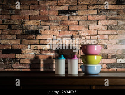 Colorful tiffin carrier and plastic bottles on wooden cupboard with vintage brick wall background against warm light Stock Photo