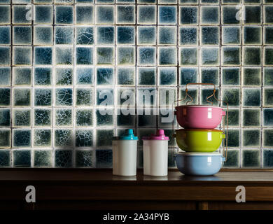 Colorful tiffin carrier and plastic cans on wooden cupboard in kitchen room with vintage tiles wall background Stock Photo