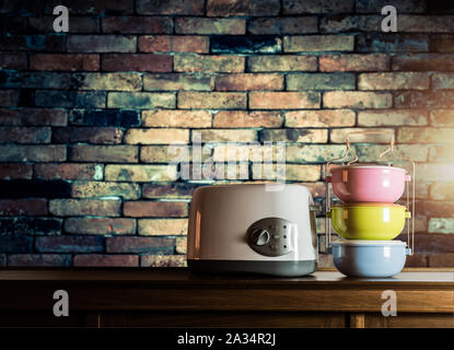 Colorful tiffin carrier and toaster on wooden cupboard with old brick wall background against warm light Stock Photo