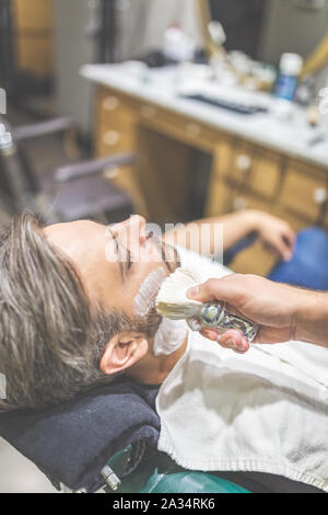 Fashionable man client during beard shaving in barber shop. Stock Photo