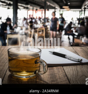 Hot tea with notebook and pen on wooden table in the coffee shop under light Stock Photo