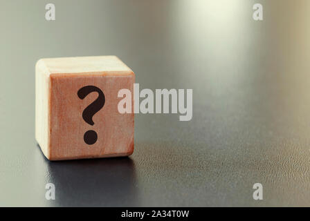 Small wooden toy block with question mark over a grey background with highlight and copy space in a conceptual image Stock Photo