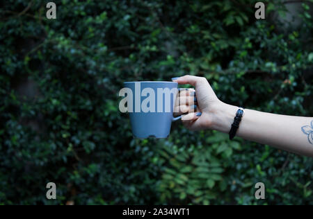 Mockup of female hand holding a coffee cup on natural garden background Stock Photo