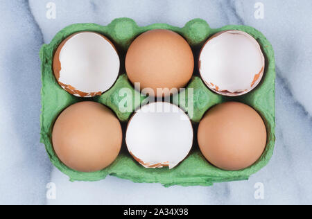 Studio shot of cracked, empty chicken egg shells in an egg box on a marble background - John Gollop Stock Photo