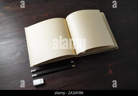 Opened book or booklet with blank kraft paper pages, pencils and eraser on wood table background. Stock Photo