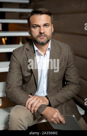 Mid-aged confident businessman in formalwear sitting on stairs Stock Photo