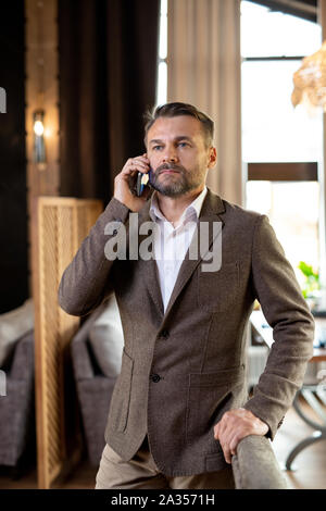 Serious agent with mobile phone listening to his client while standing by table Stock Photo