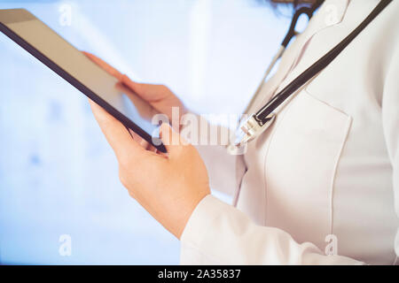Woman doctor using tablet computer while standing straight in hospital Stock Photo
