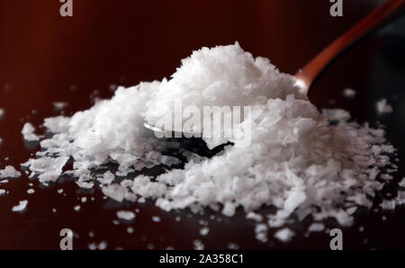Sea salt flakes in spoon on back-lit dark background. Stock Photo