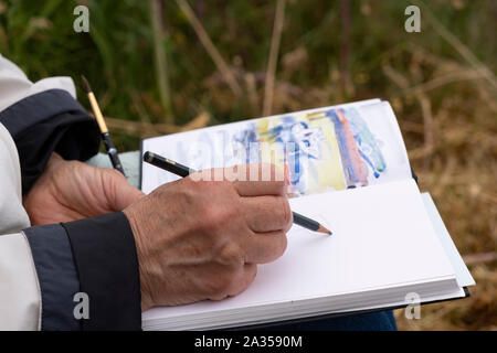 Hand drawing in sketchbook, enjoying retirement drawing outside wearing casual warm clothing Stock Photo