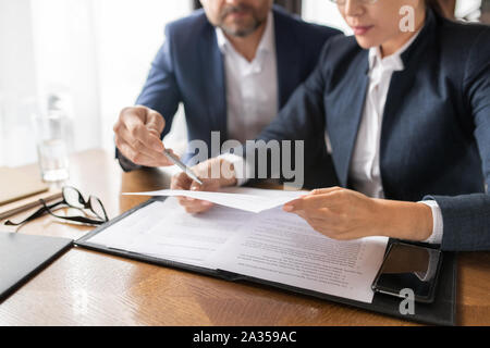 Contemporary businessman pointing at paper held and read by young Asian woman Stock Photo