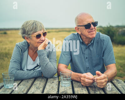 A senior couple are sitting at a picnic table outdoors in the countryside Stock Photo
