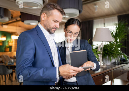 Two serious colleagues in formalwear reading electronic document in touchpad Stock Photo