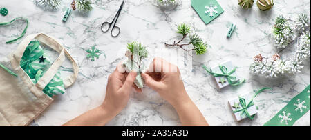 Wintertime, creative flat lay with various winter craft supplies, christmas tree twigs and hands decorating gift boxes. Flat lay on marble, panoramic Stock Photo