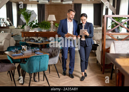 Two business partners walking along restaurant and discussing online data Stock Photo