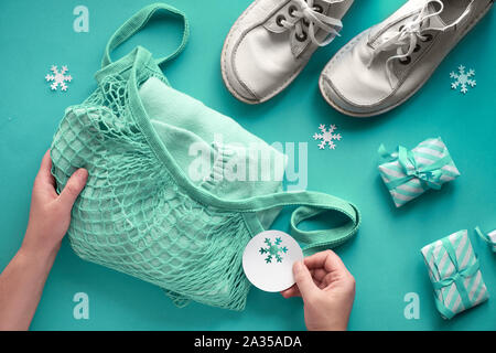 Packing presents, blue sweater in string bag, or mesh bag. Wintertime composition, flat lay on blue paper with small wrapped gifts and snowflakes. Chr Stock Photo