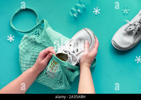 Packing presents, blue sweater in string bag, or mesh bag. Wintertime composition, flat lay on tile paper with snowflakes. Christmas gifts packed in e Stock Photo
