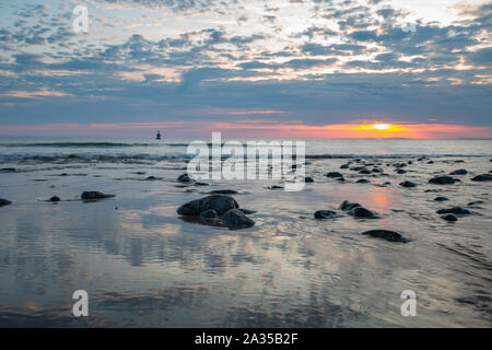 Sea waves washing out rocky shore reflecting colourful sunset sky in Barmouth, UK Stock Photo