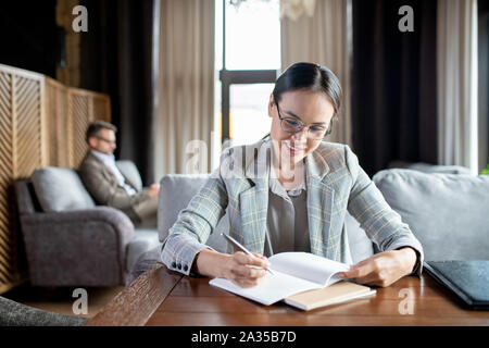 Happy young female student making notes in copybook while preparing for lesson Stock Photo