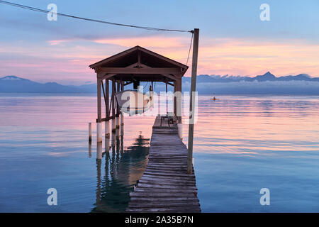 A boat is suspended above the Caribbean Sea and a kayaker paddles by on the island of Utila in Honduras Stock Photo