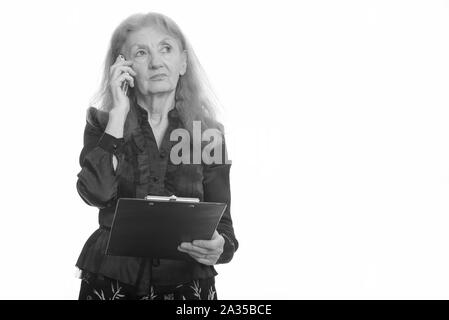 Studio shot of senior businesswoman holding clipboard while talking on mobile phone while thinking Stock Photo