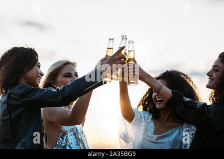 Multi-ethnic friends toasting beers at sunset. Women celebrating with beers in the evening. Stock Photo