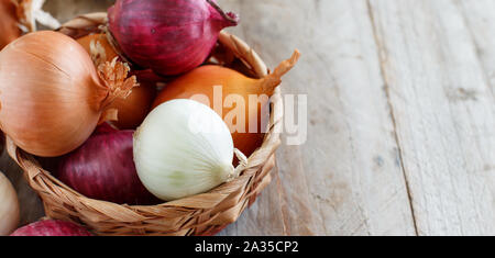 Raw onions in a basket on a wooden table Stock Photo