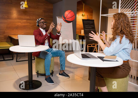 Two happy young multicultural students of college playing with ball in cafe Stock Photo