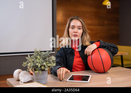 Pretty young casual student with ball and digital tablet sitting in college cafe Stock Photo