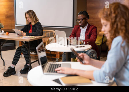 Group of multicultural students using mobile gadgets while preparing homework Stock Photo