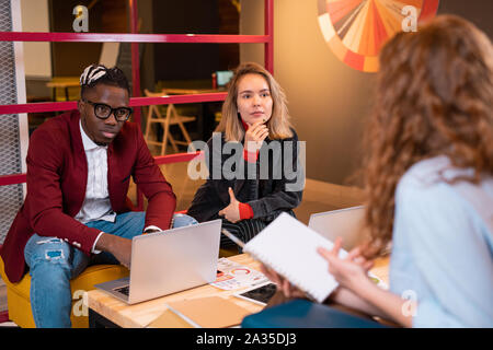 Two serious multicultural students listening to groupmate during discussion Stock Photo