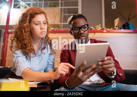 Two young intercultural employees in casualwear discussing electronic document Stock Photo