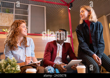 Three young cheerful managers discussing working questions at meeting Stock Photo